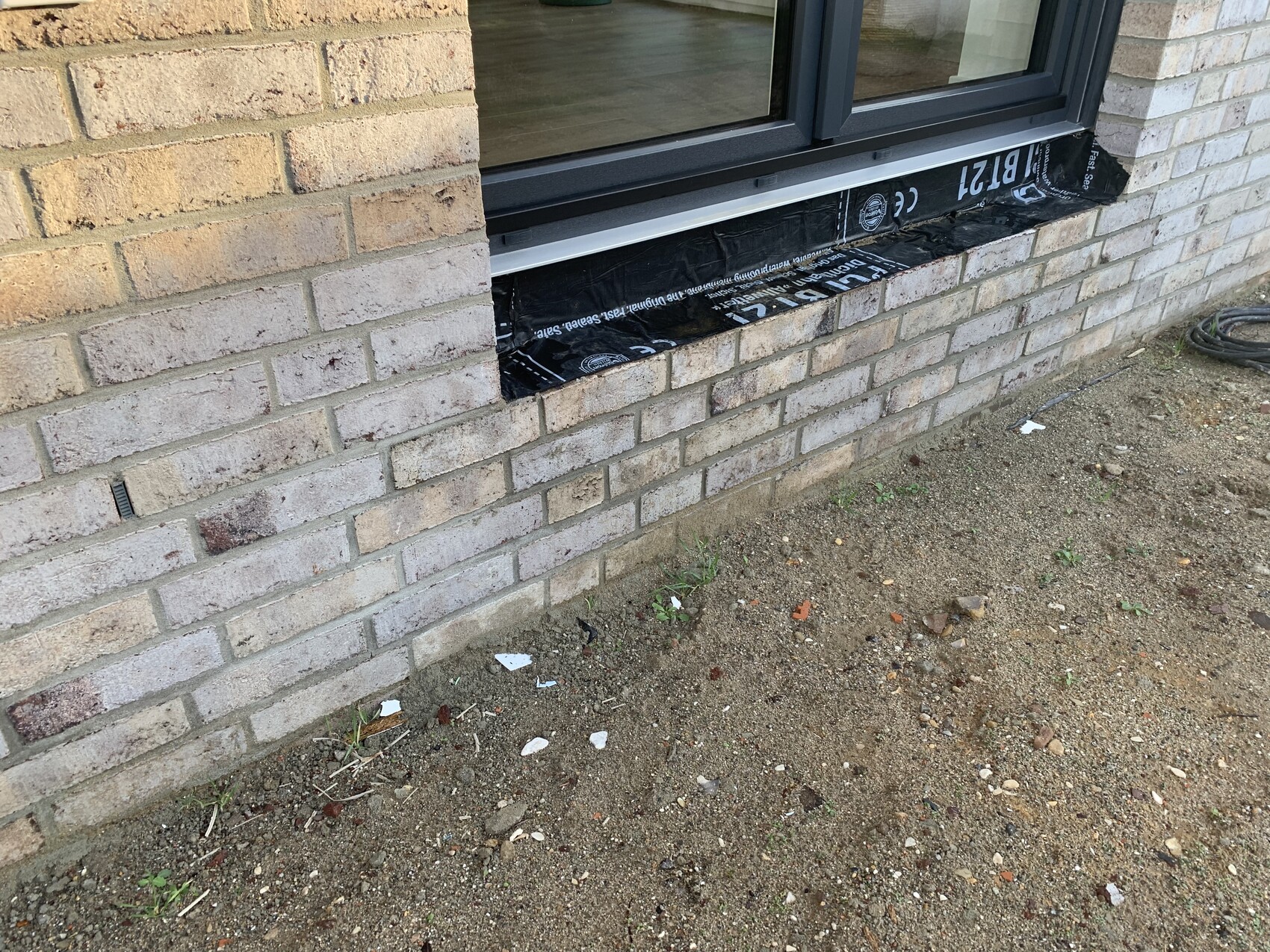 Exterior wall made of light bricks; window with black sealing tape underneath.