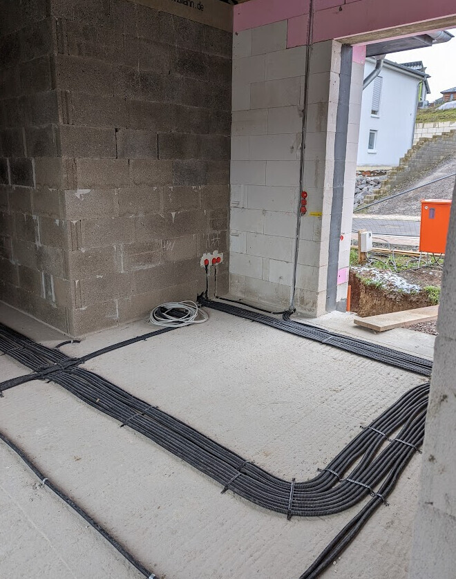 Construction site: Black cable ducts running across the floor, red sockets on unfinished concrete wall.