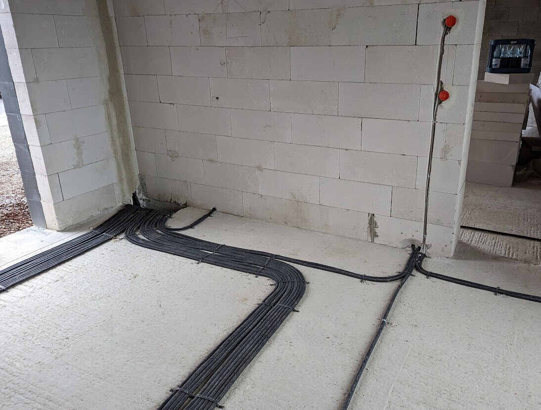 Construction site: Floor with black cable ducts, concrete wall; visible installations.