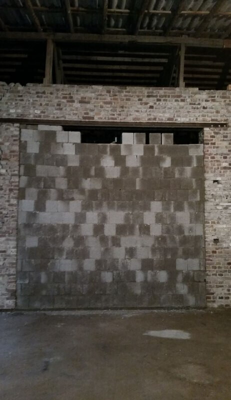Large gray block wall in front of a brick hall; ceiling with exposed wooden beams.