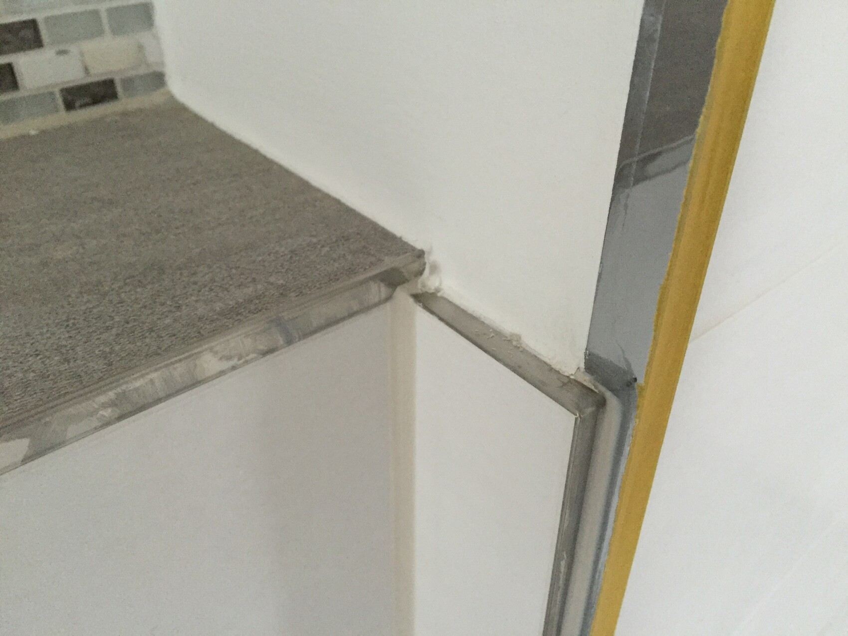 Bathroom shower with metal frame, tiles, and visible yellow protective edge