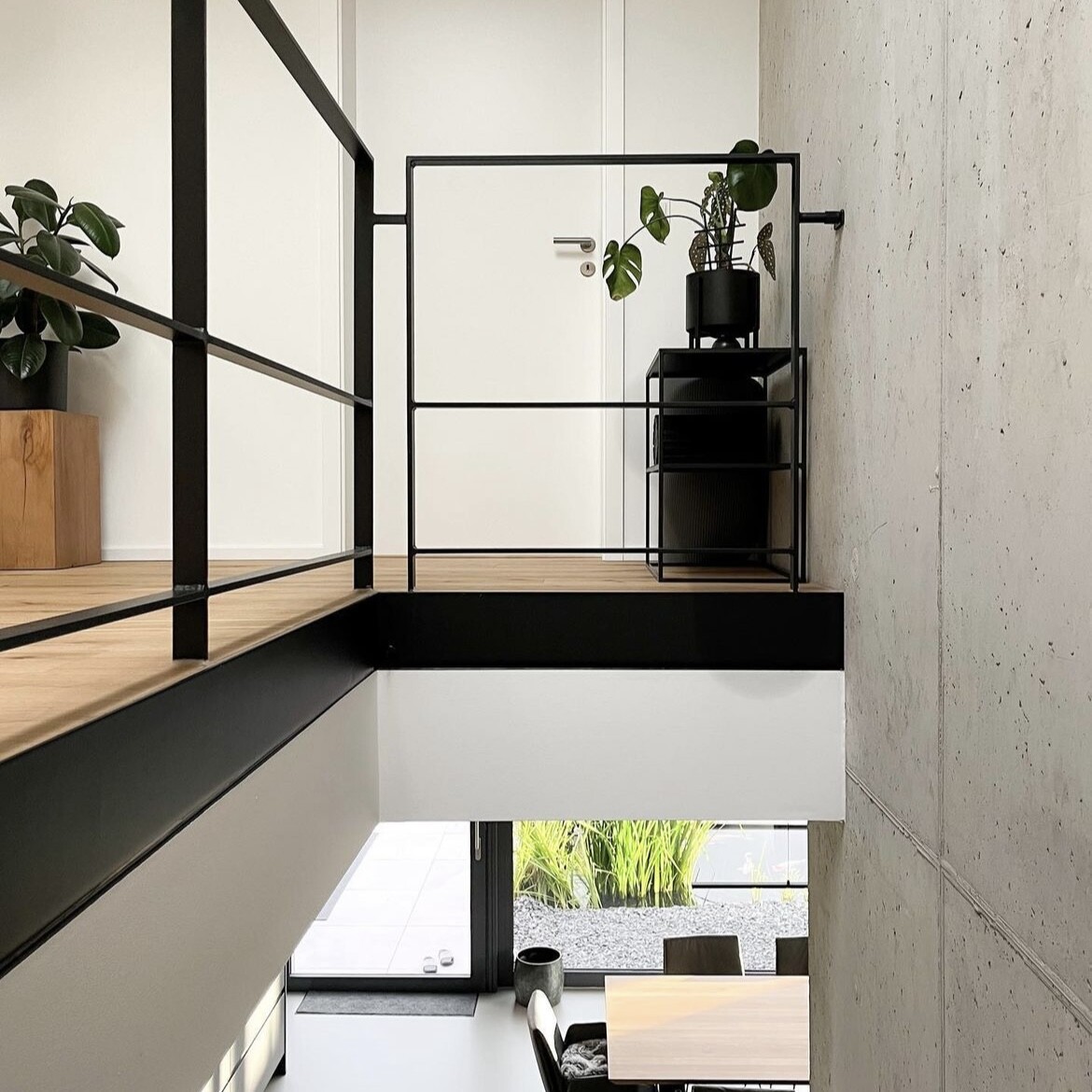 Modern loft gallery with black metal railing, plant pot, and wooden floor.