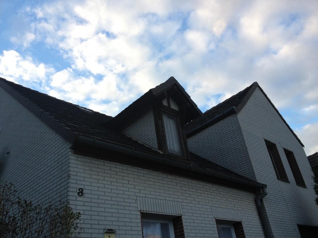 White brick house with dormer and dark roof against a blue sky
