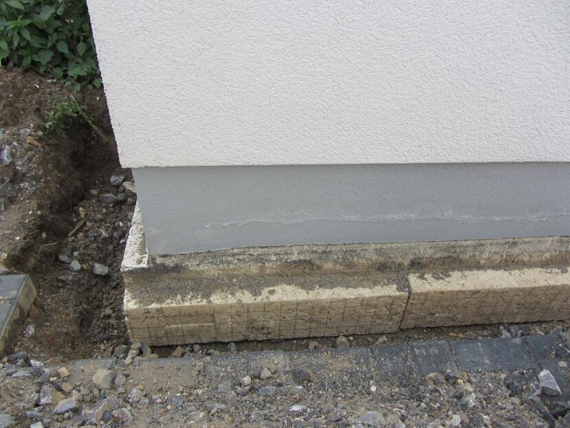 Exterior wall with render, foundation slab on ground, gravel and soil visible