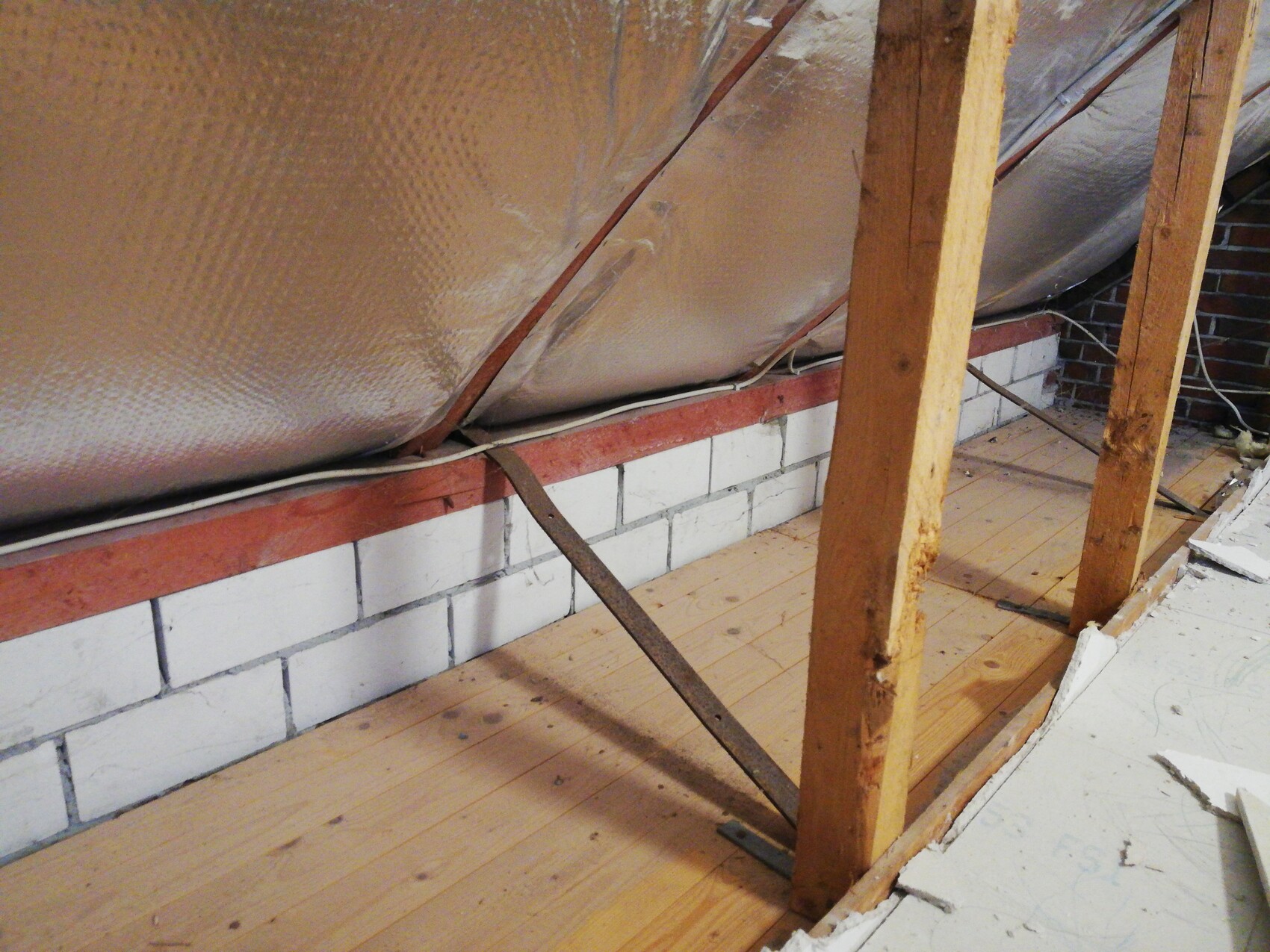 Attic with insulation foil, wooden studs, diagonal metal brace, and wooden floor.