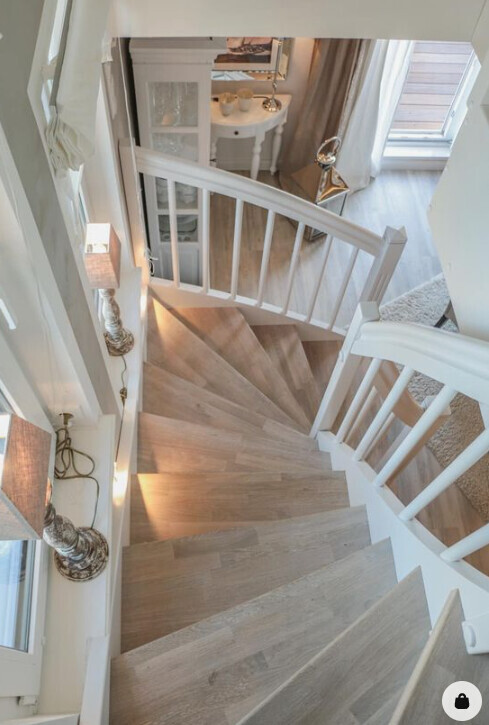 Bright wooden staircase with white railing, interior with light furniture in the background.