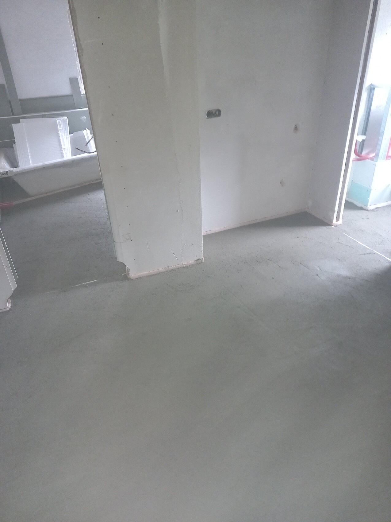 Interior of a construction site: smooth concrete floor, white walls with recessed opening, building materials on the left.
