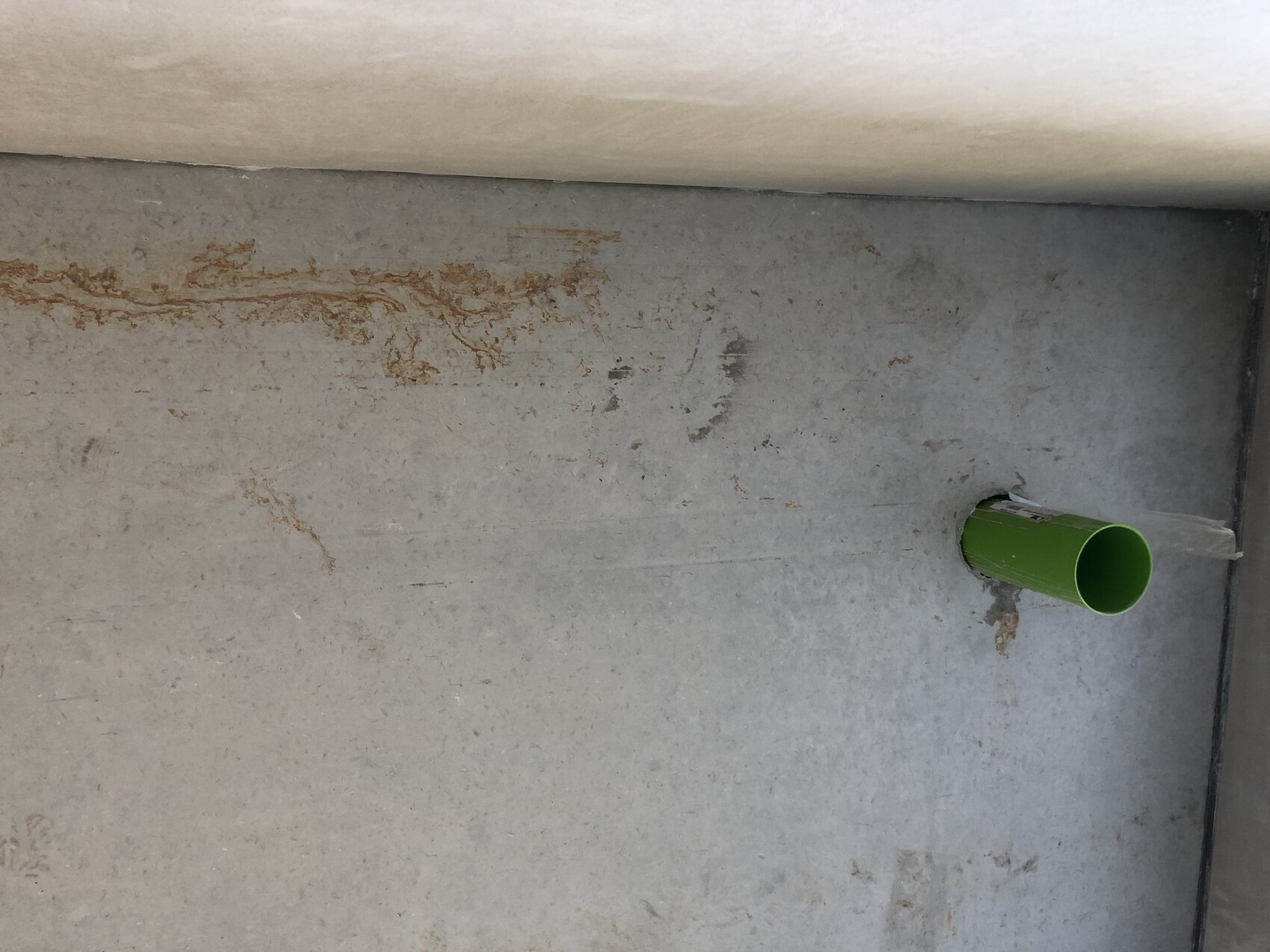 Green pipe protrudes from gray concrete wall; rust stains on masonry.