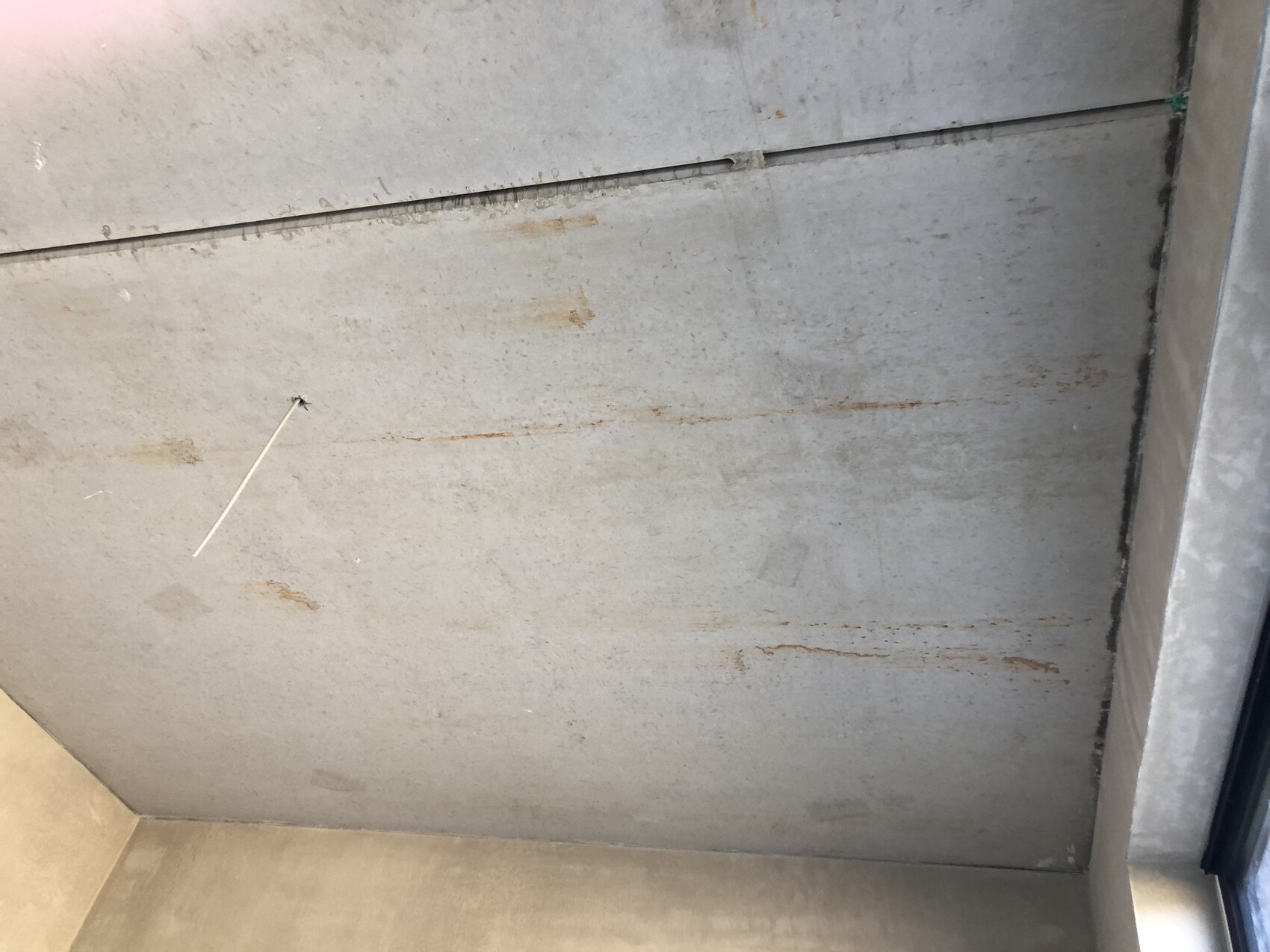 Rough concrete ceiling with rust stains; a thin white cord protrudes from a hole.