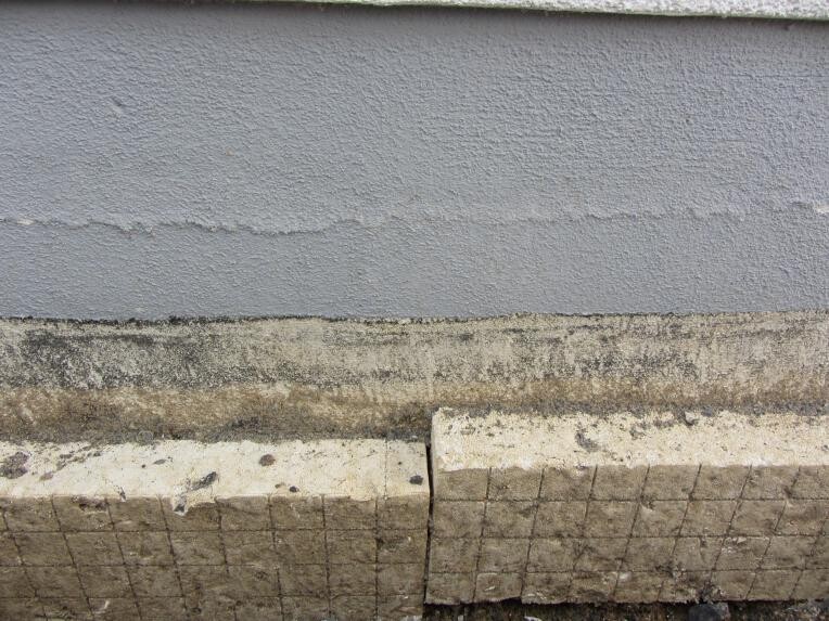 Shell wall with plaster cracks and foundation slabs visible on the ground