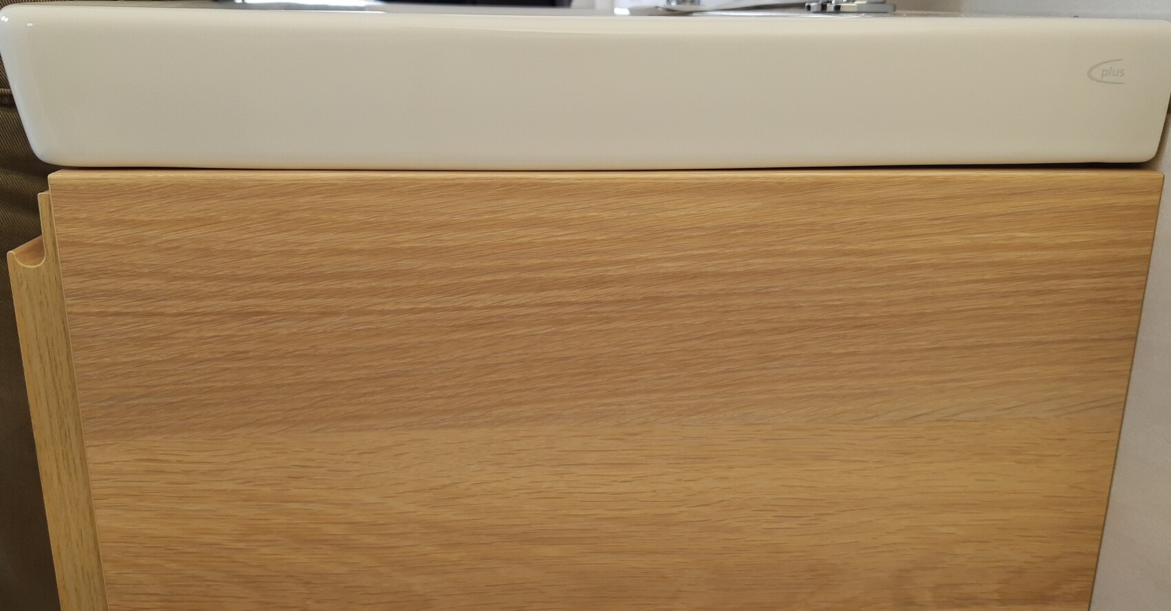 White rectangular washbasin on a light wood base cabinet.
