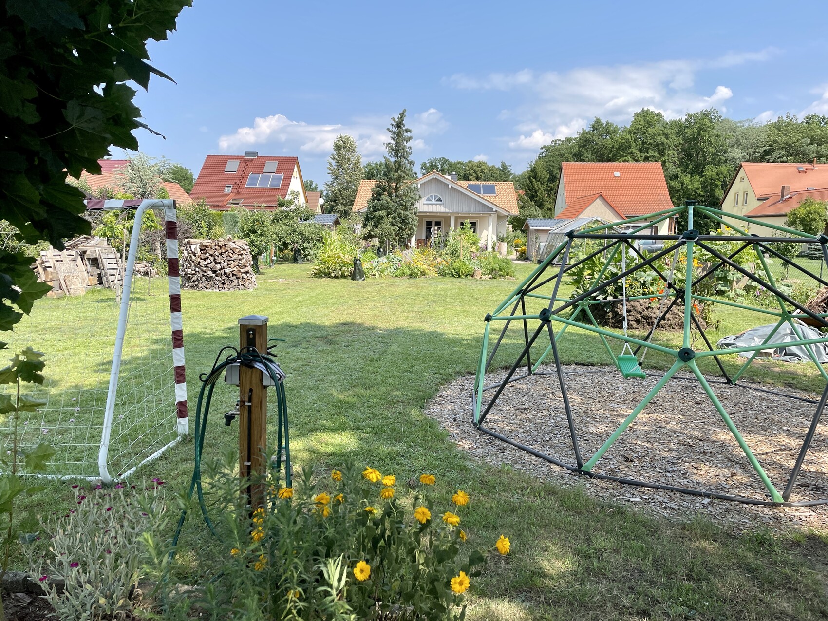 Garten mit grünem Geodome-Klettergerüst und Schaukel; Häuser im Hintergrund.
