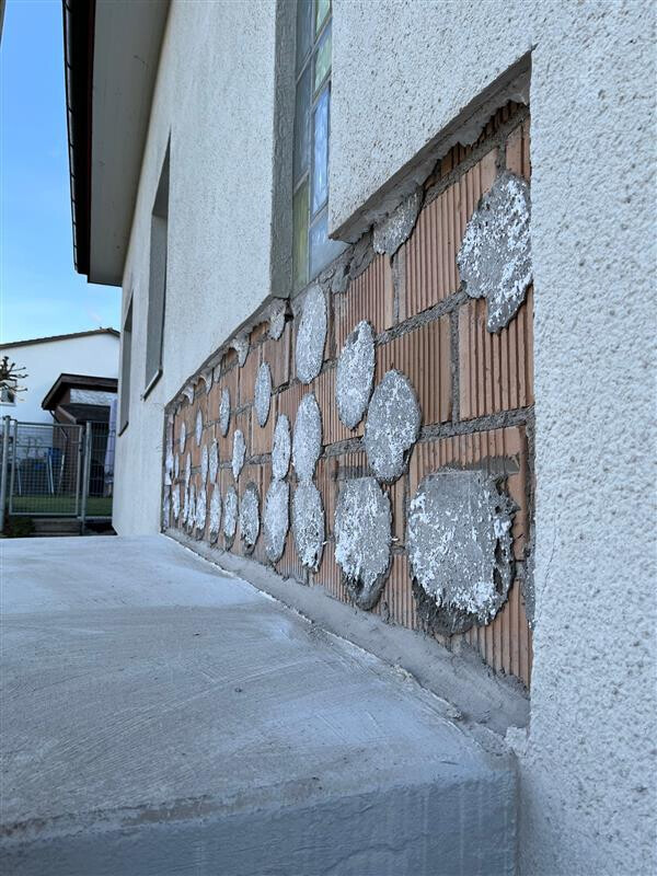 Exterior wall of a building with round cement patches on brick above a concrete ramp.
