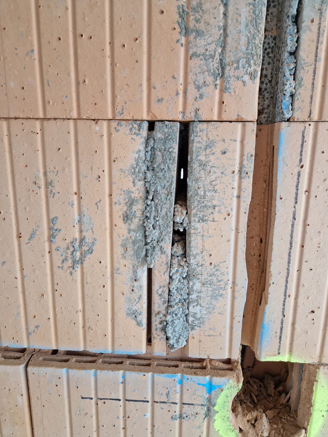 Close-up of damaged brick wall with vertical gap, cement mortar and paint splashes.