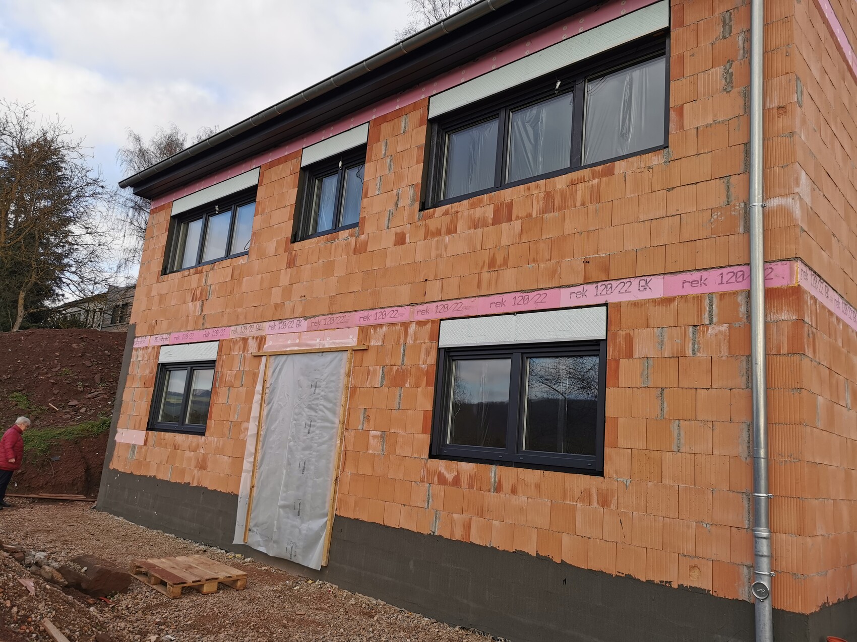 Two-story shell construction house made of orange brick with black windows and entrance covered with plastic.