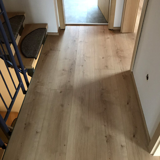 Bright hallway with wooden floor, staircase on the left, open passage to the next room.