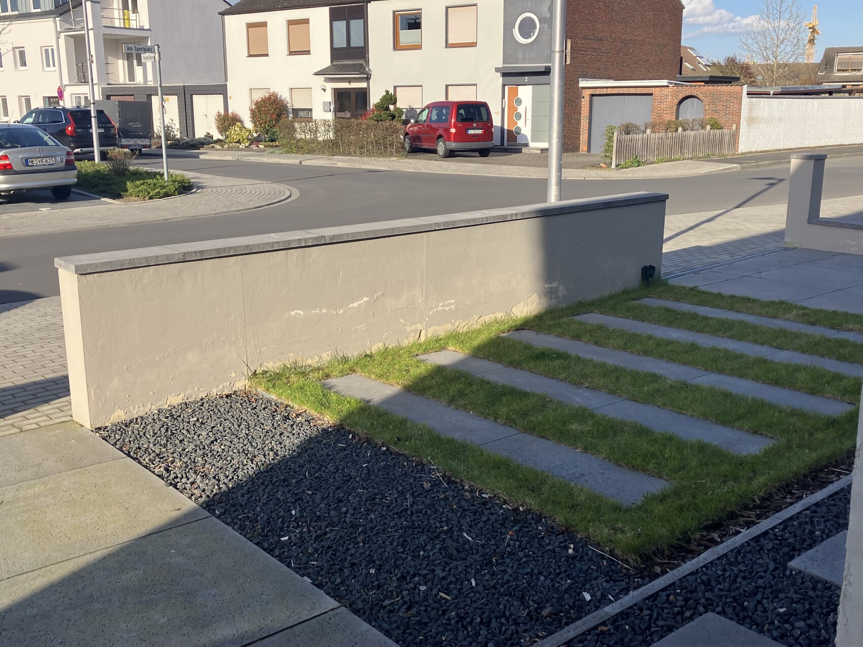 Front view of a front yard with concrete wall, strip of grass and paving stones, street in the background.