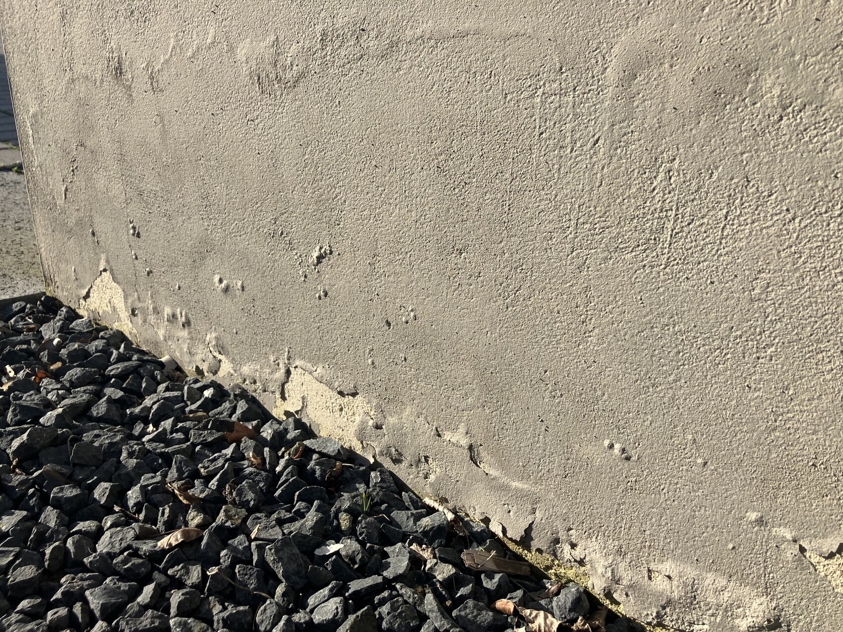 Beige wall with cracked plaster; at the bottom a pile of gray stones and gravel.