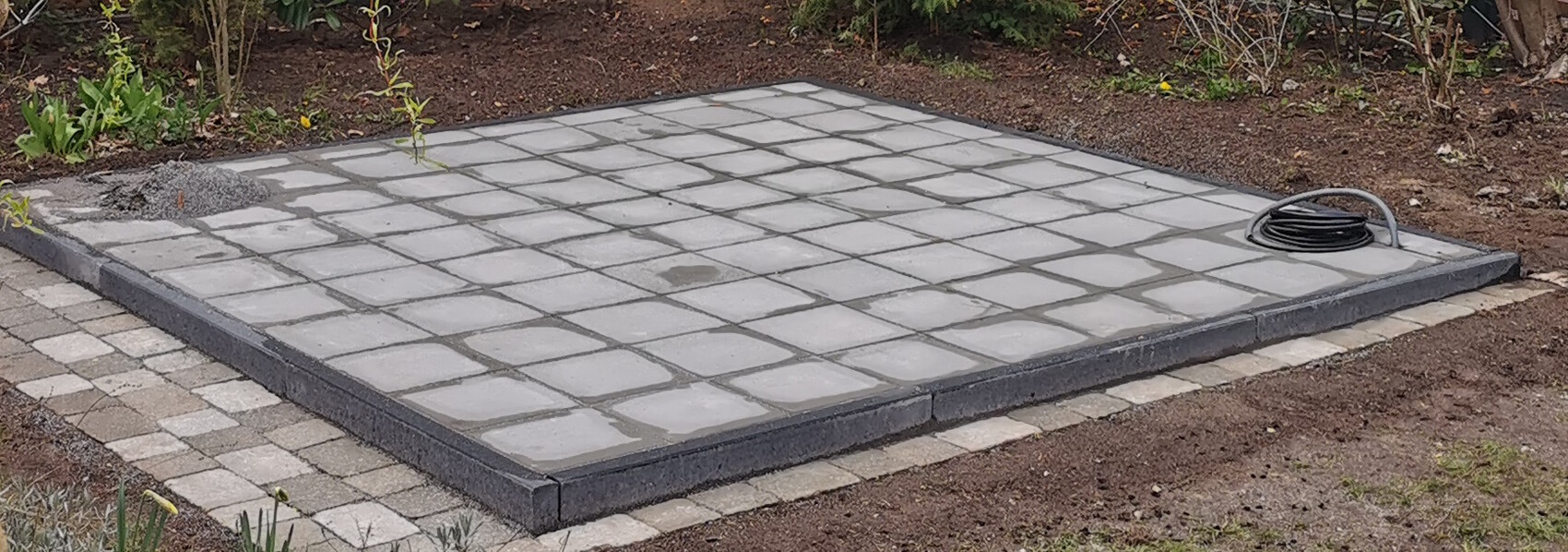 Paved terrace made of square paving stones in the garden; cable reel on the right.