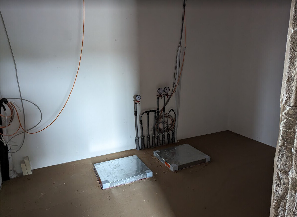 Utility room with pipes, measuring instruments, cables; two metal plates on the floor.