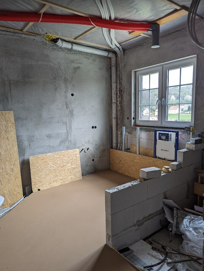 Construction site: bathroom base with pipes, OSB boards, Geberit flush tank, and window.