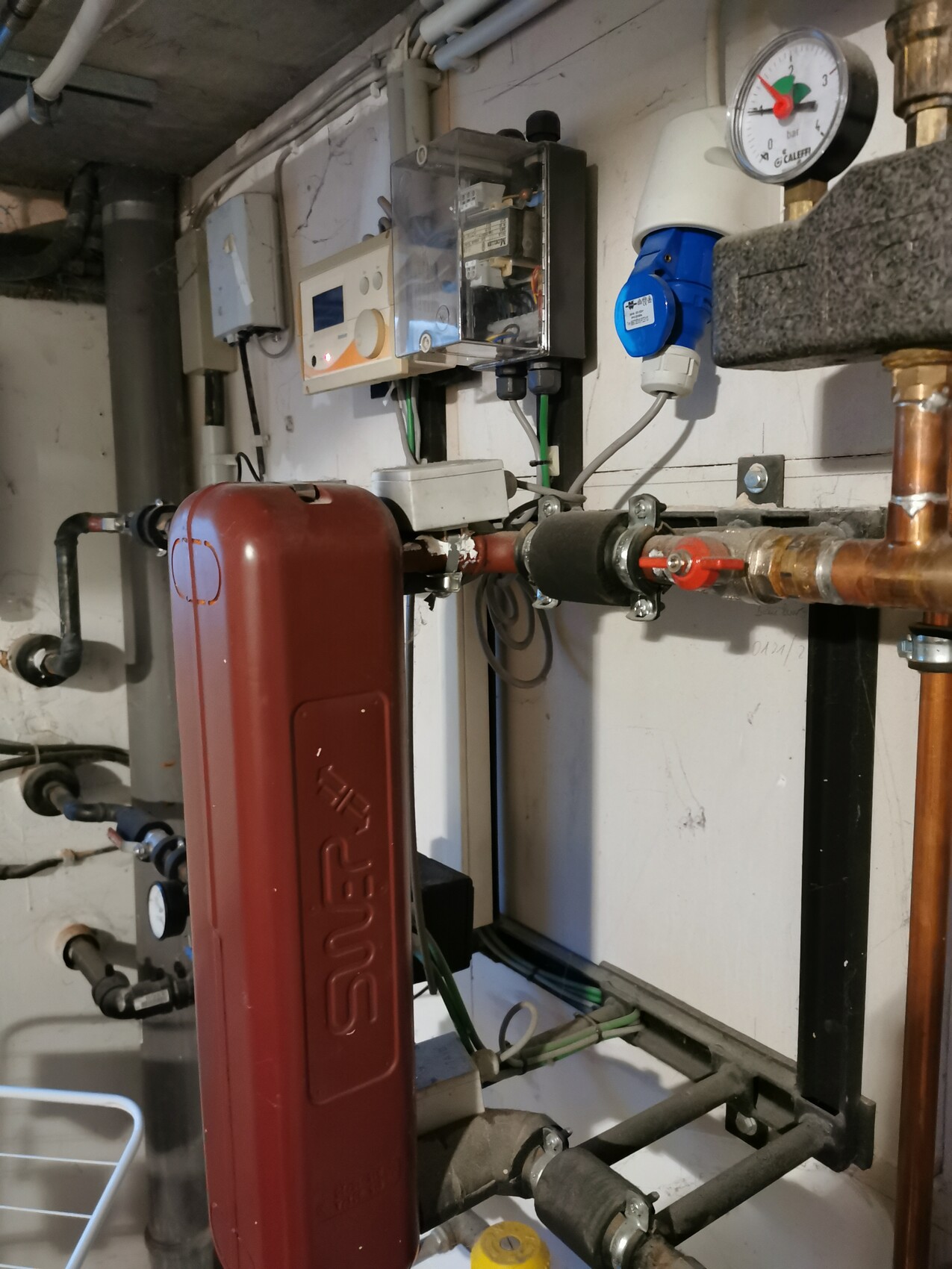 Heating system with red expansion tank, copper pipes, pressure gauge and control unit.