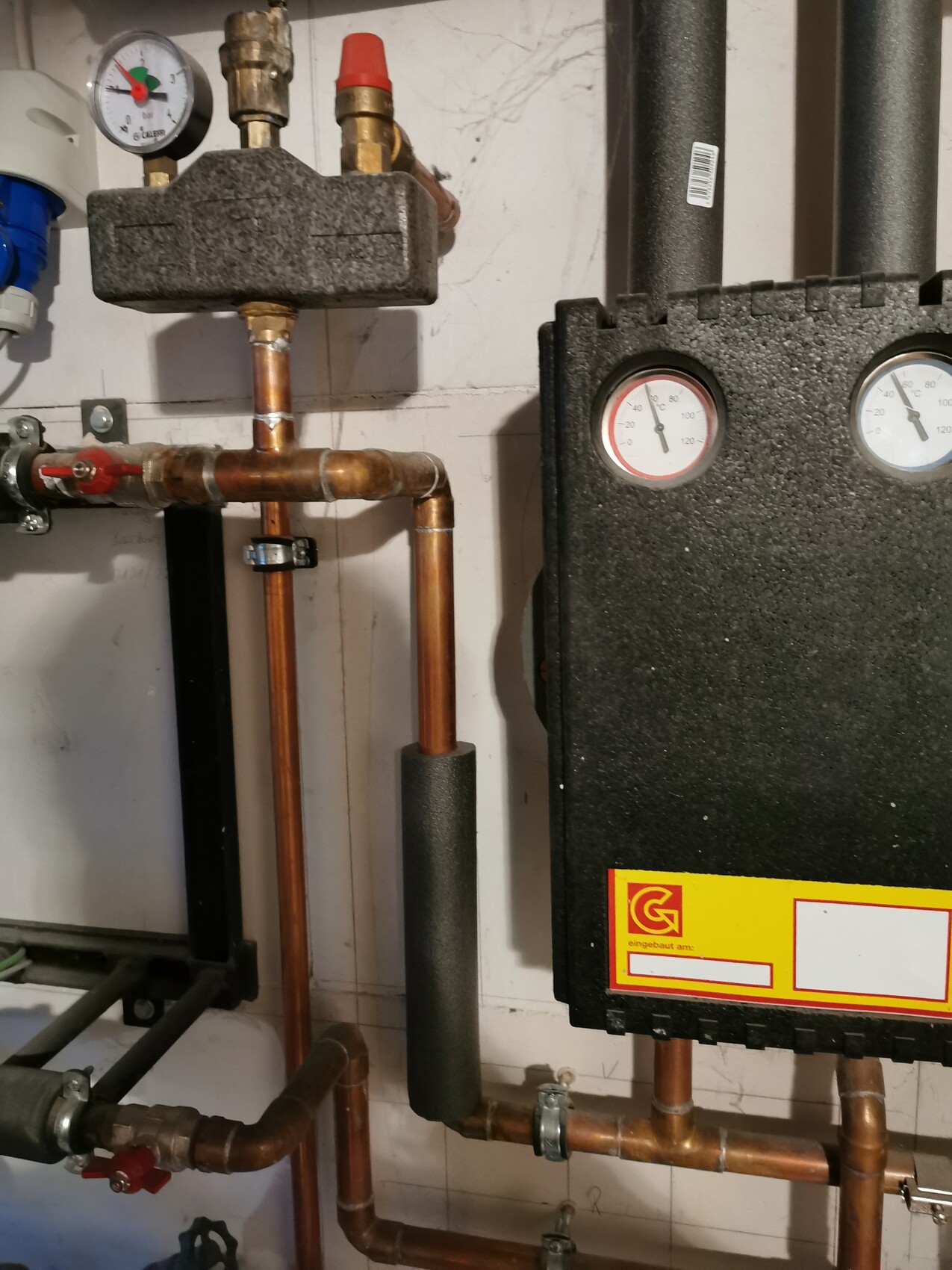 Heating system with copper pipes, pressure gauge and insulated pipework.