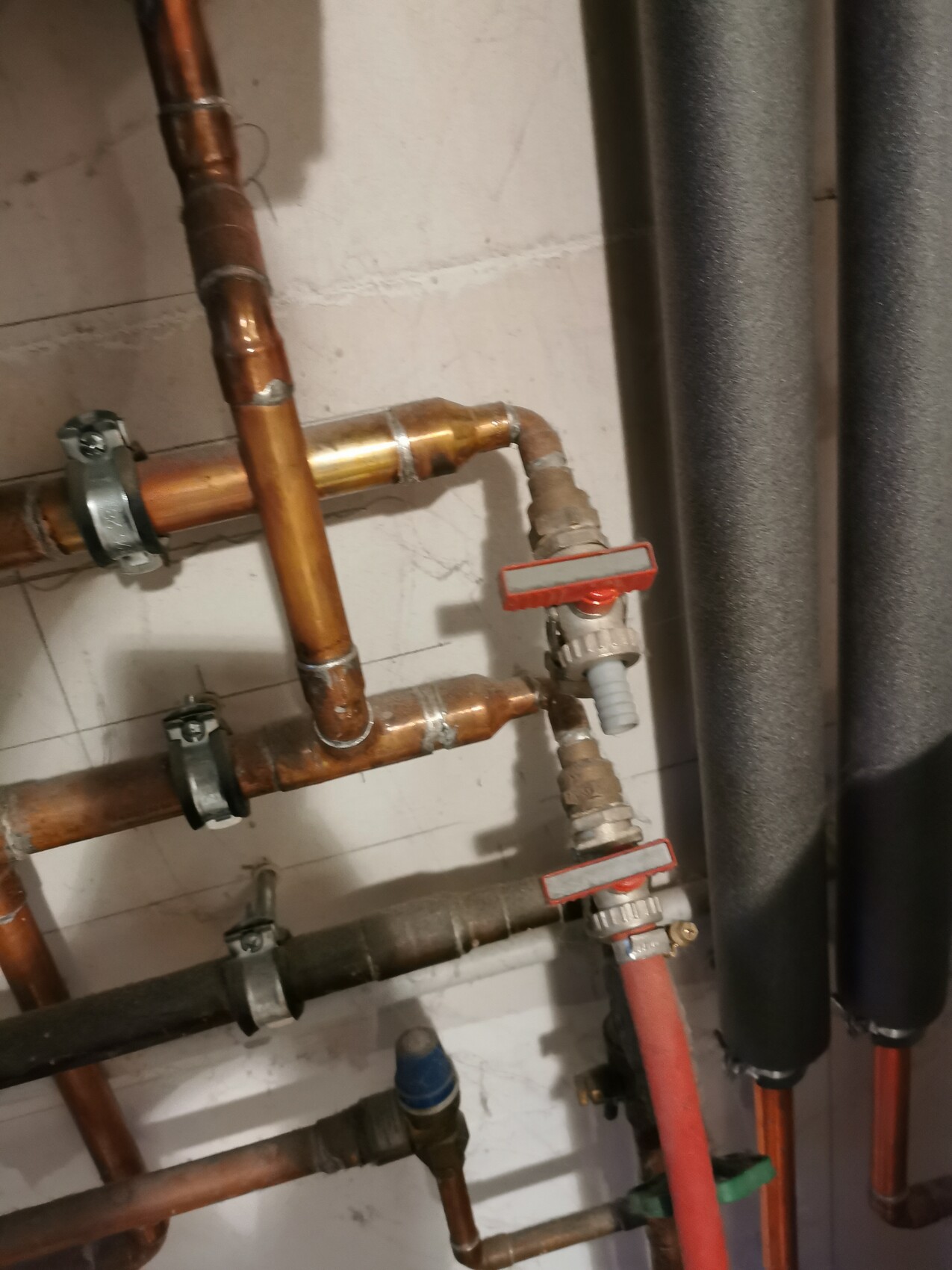 Copper pipes with red shut-off valves in a basement room.