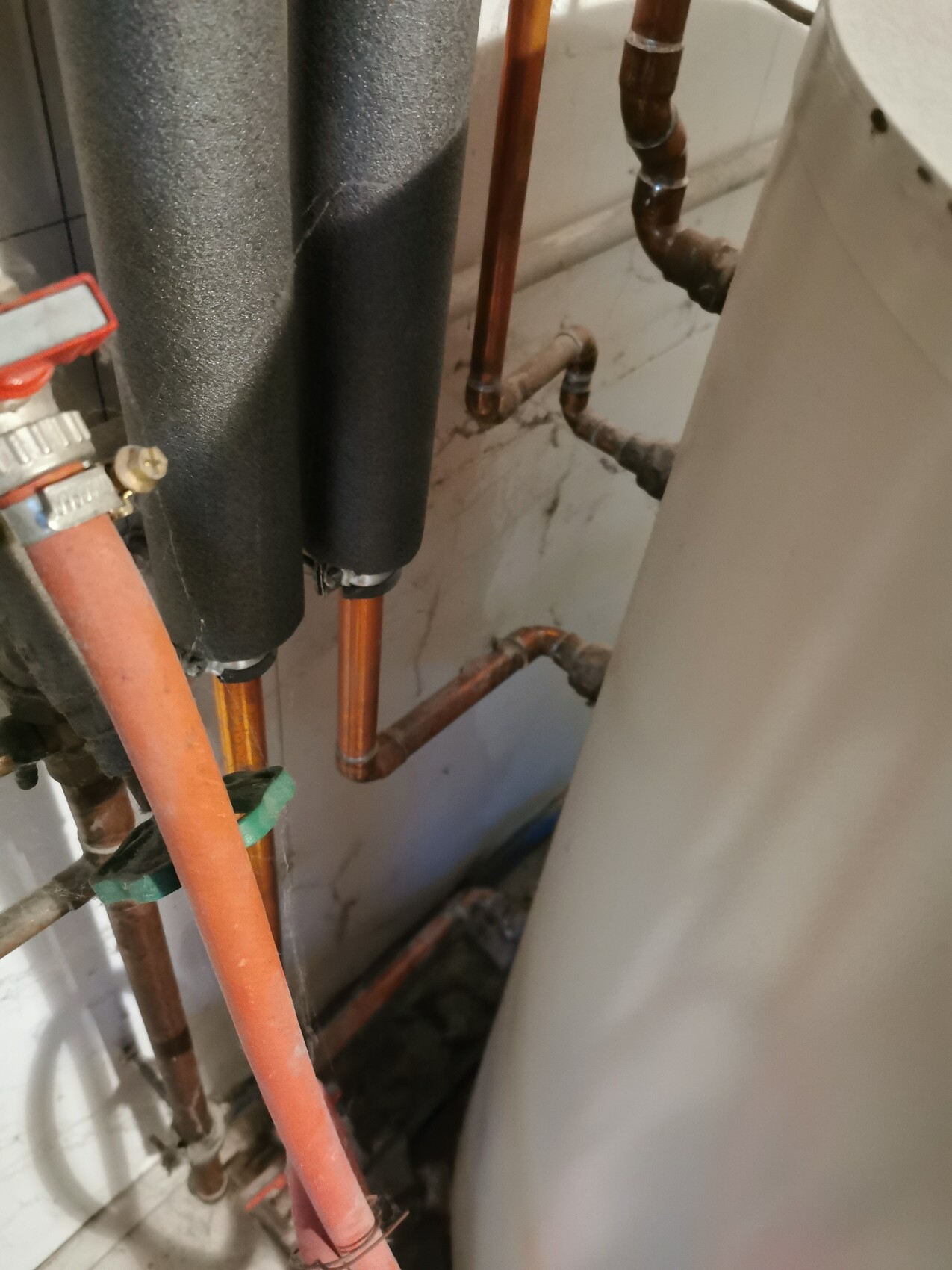 Copper pipes with black insulation, red shut-off valve and hot water boiler in basement.