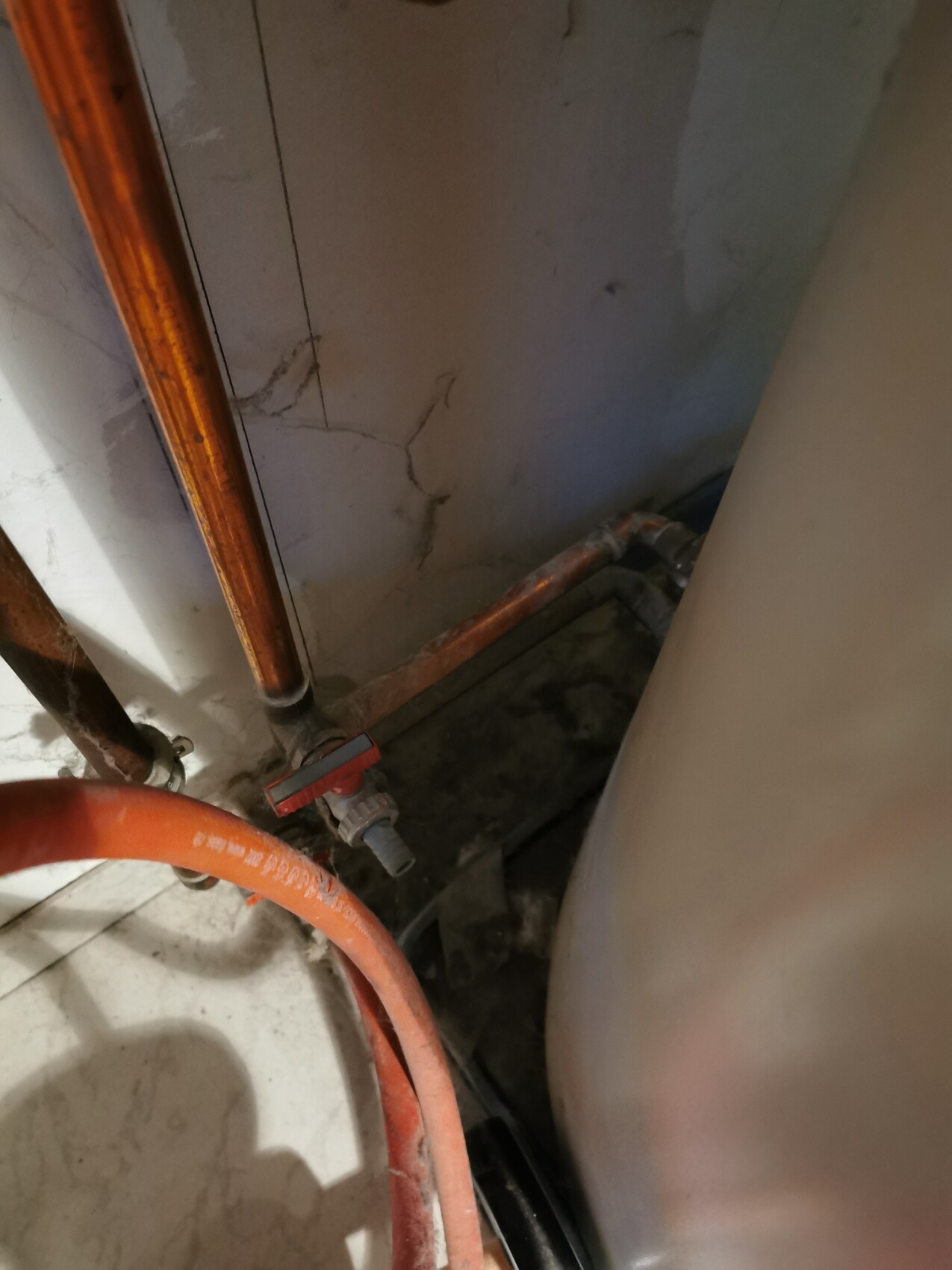 Basement room with copper pipes, red shut-off valve, orange hose next to a water heater.