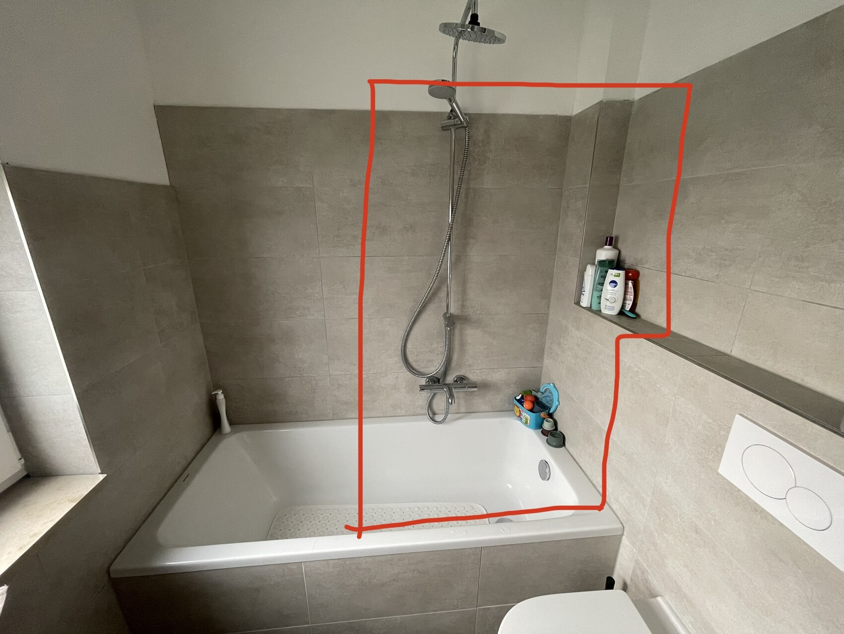 Bathroom with bathtub and shower, gray tiles, hygiene accessories on shelf.