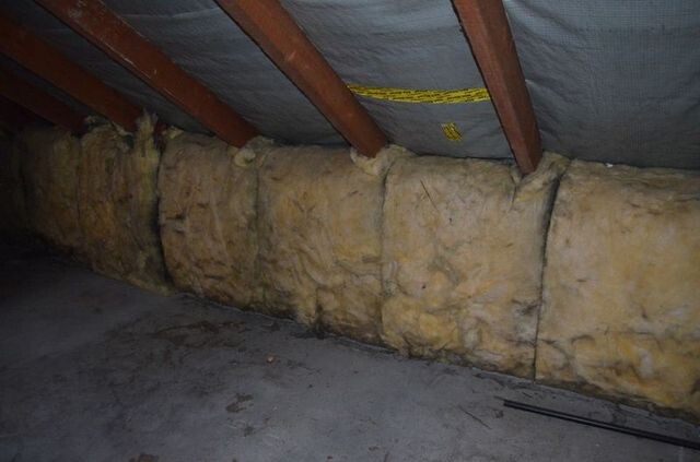 Gelbe Glaswolle-Dämmung zwischen Holzbalken am Dachboden.