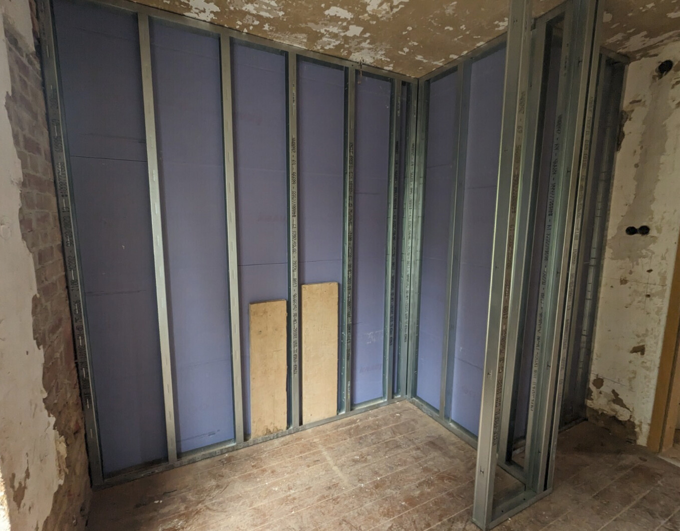 Interior construction site with steel frame wall structure and partially plastered walls.