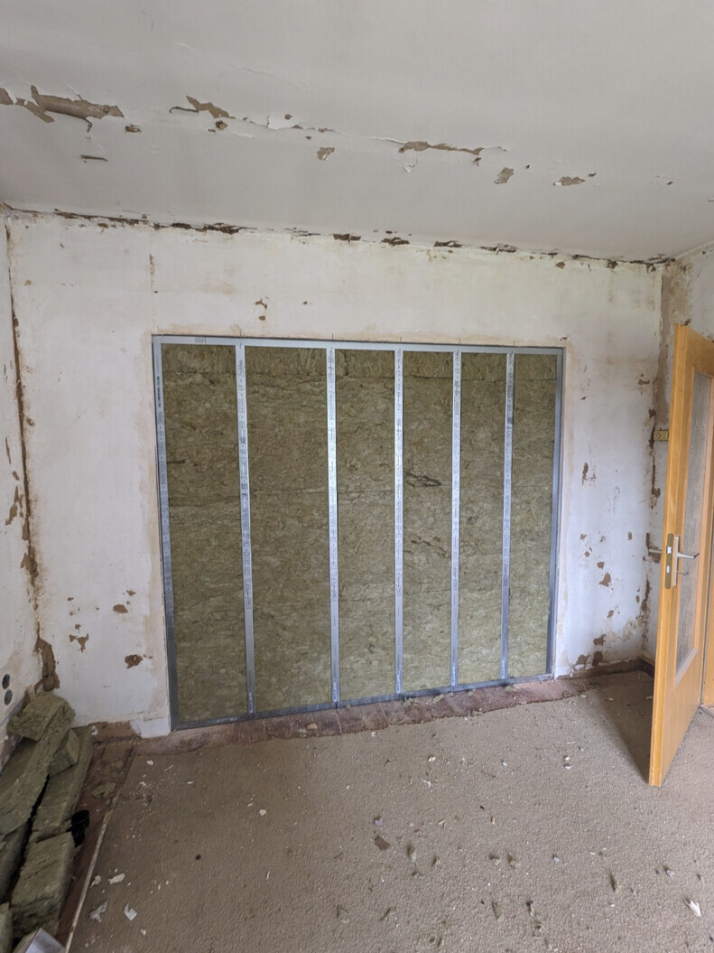 Room under renovation: exposed wall with metal stud frame and insulation, door open.