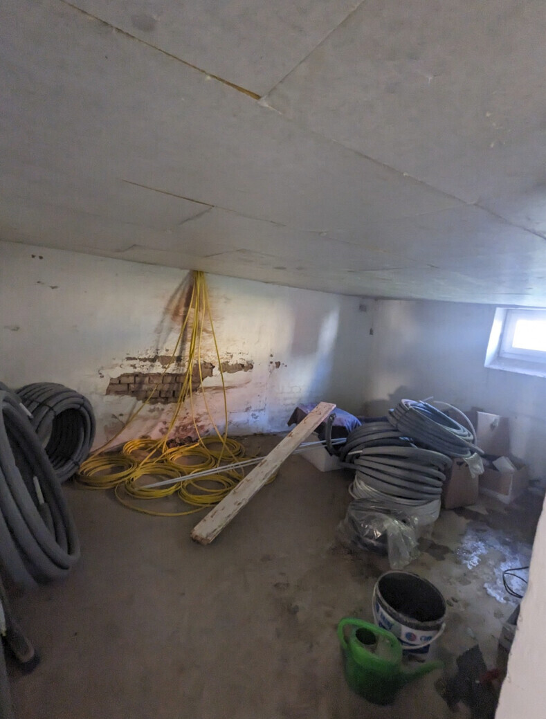 Basement room with yellow cable reels, gray hoses, wooden batten, and buckets.