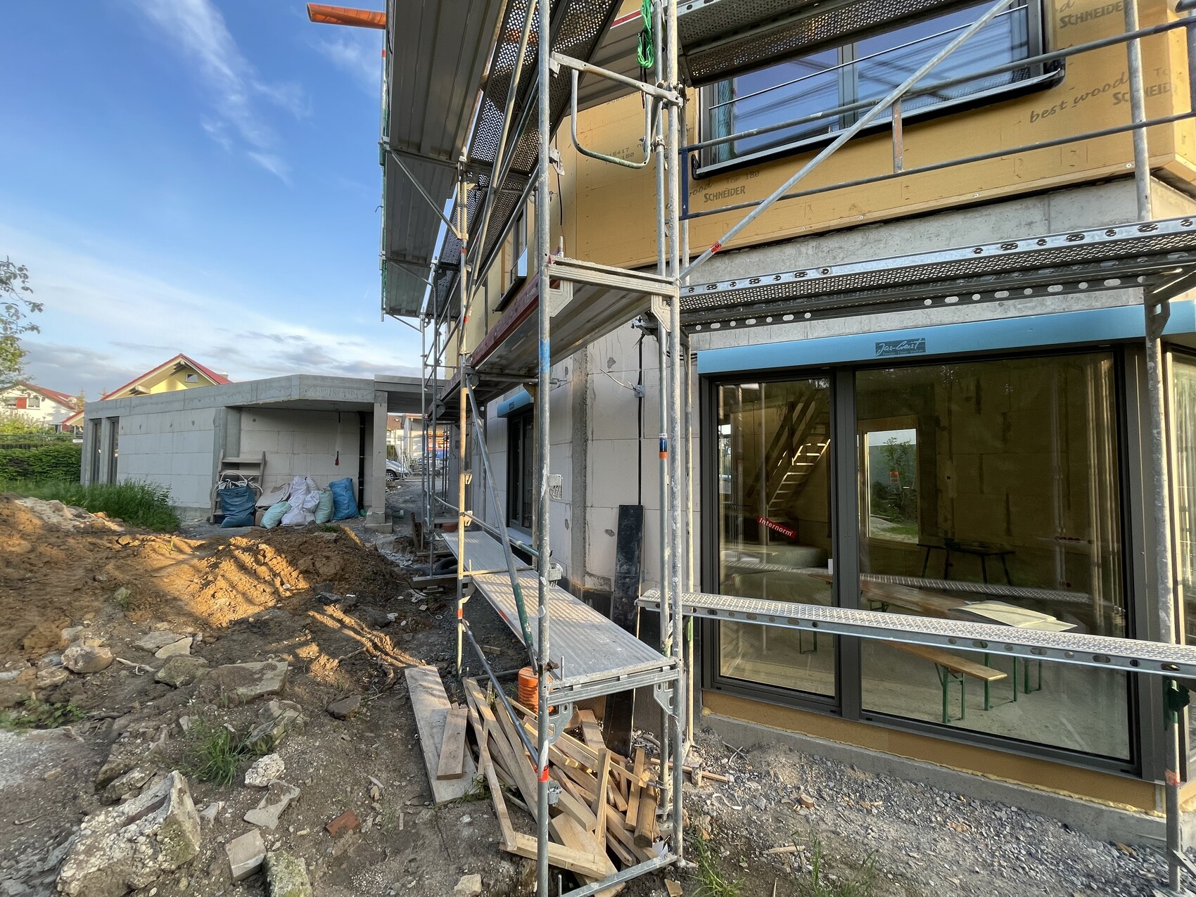 Construction site at residential building: scaffolding around yellow facade, large window fronts, and building materials.