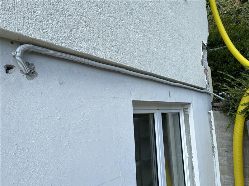 Exterior wall of a house with a horizontal cable line above the window; to the right, a yellow pipe.