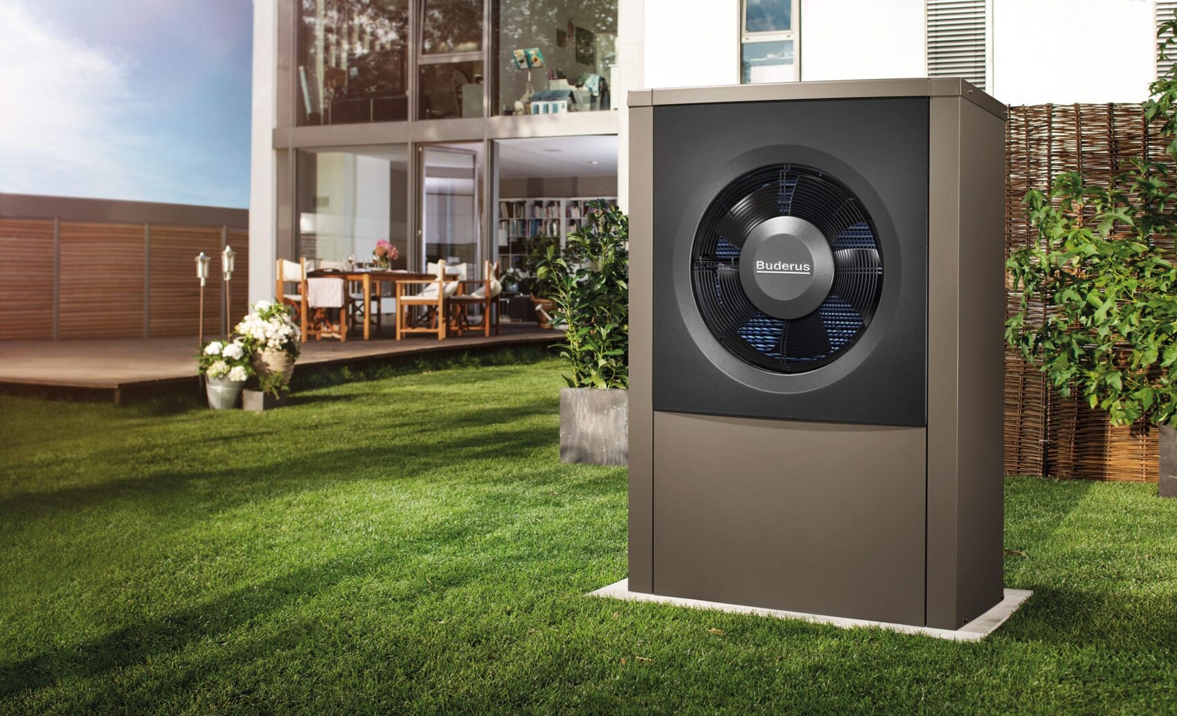 Large Buderus outdoor air conditioning unit in the garden in front of modern house facade and terrace.