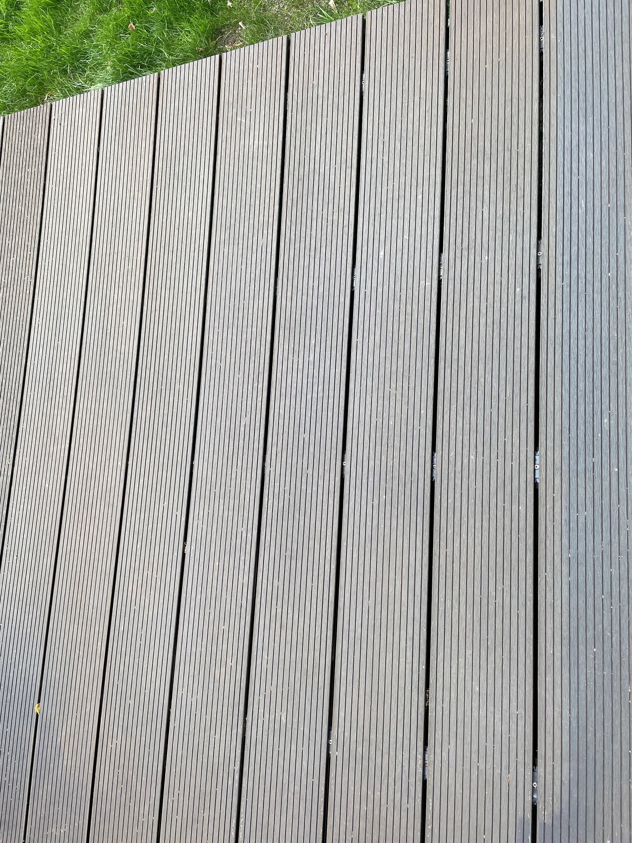 Dark wood decking boards running parallel; grass visible at the top edge.