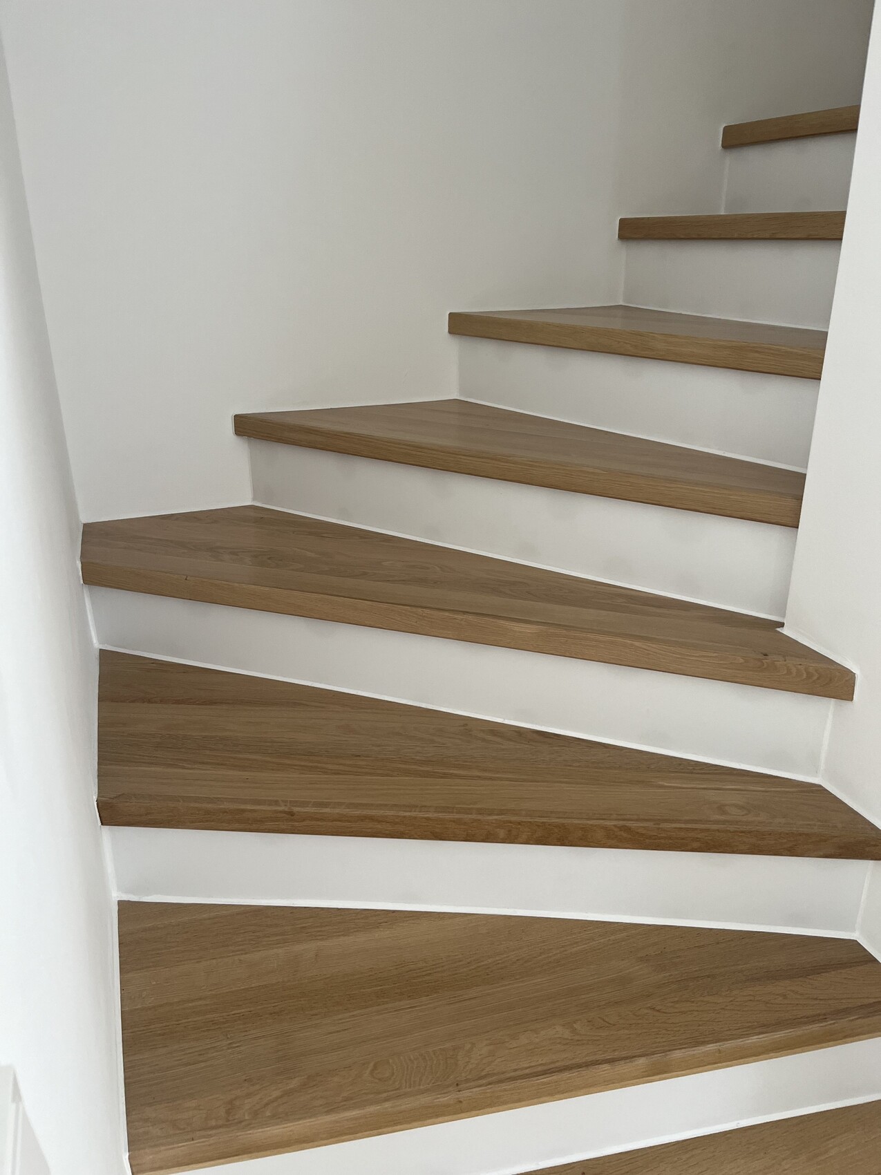 Moderne Holztreppe mit weißen Wangen in hellem Innenraum, mehrere Stufen nach oben.