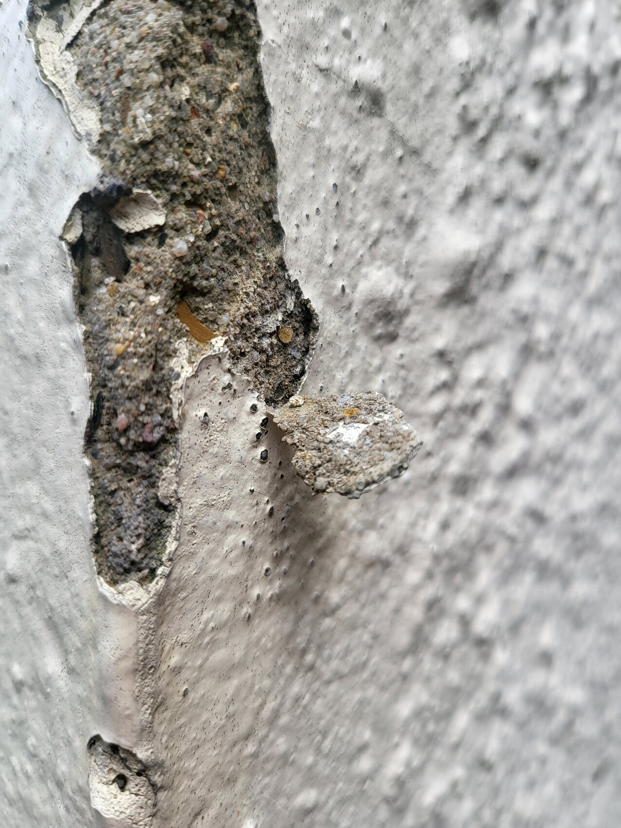 Close-up of a chipping concrete wall with exposed rock, gravel, and cement.