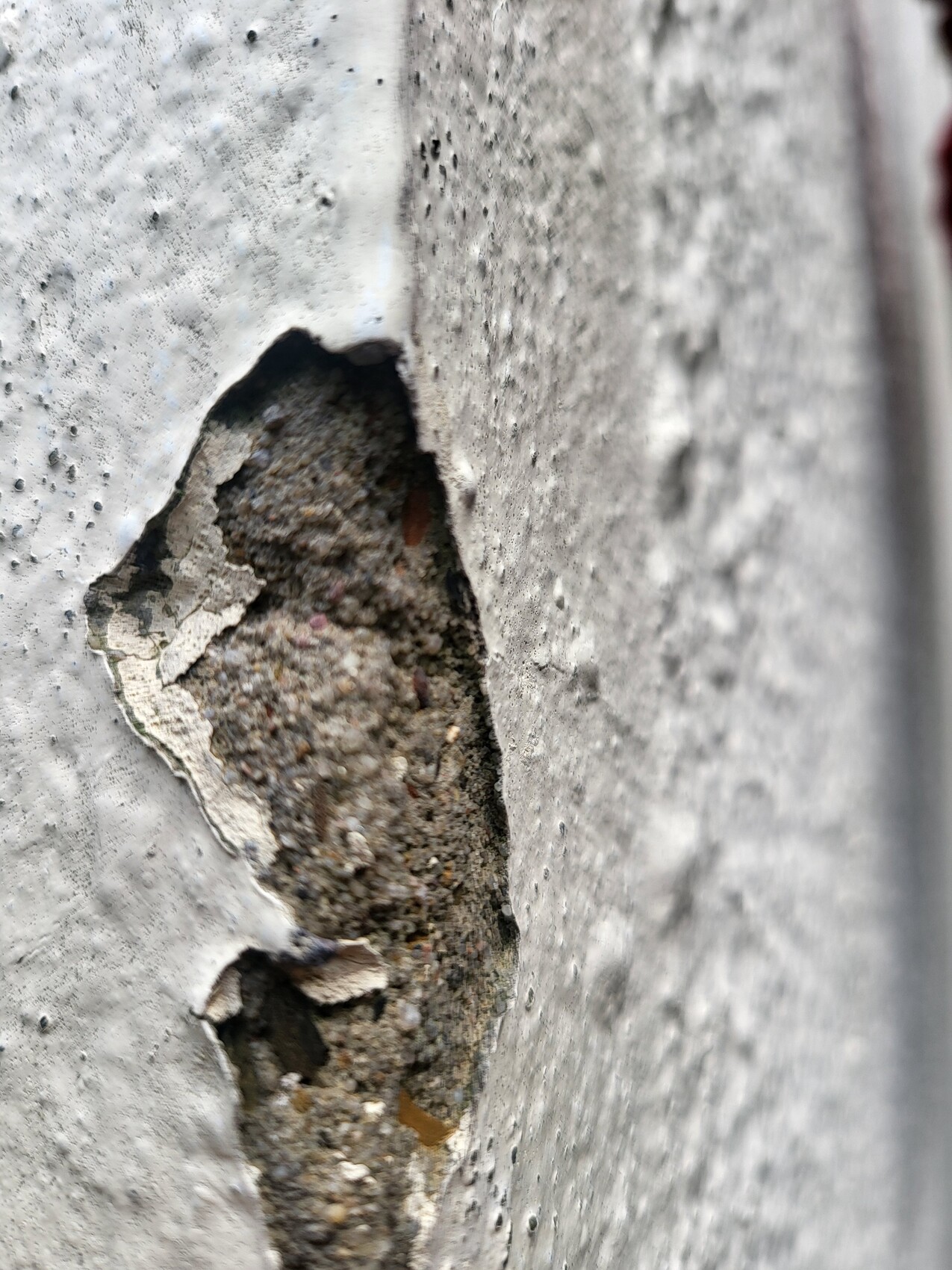 Damaged concrete wall with hole; interior shows gravel and sand.
