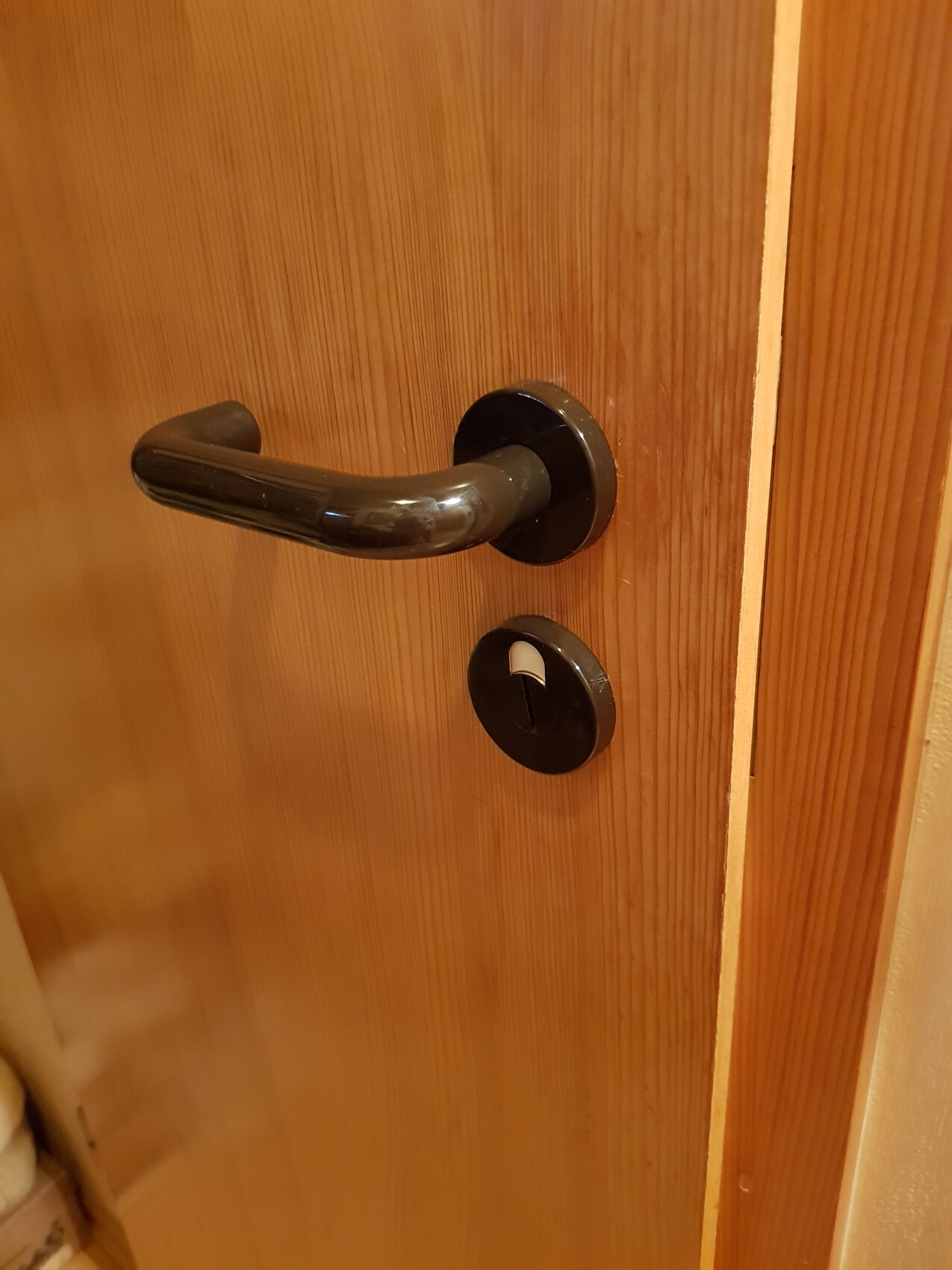 Wooden door with black metal door handle and round escutcheon with keyhole.