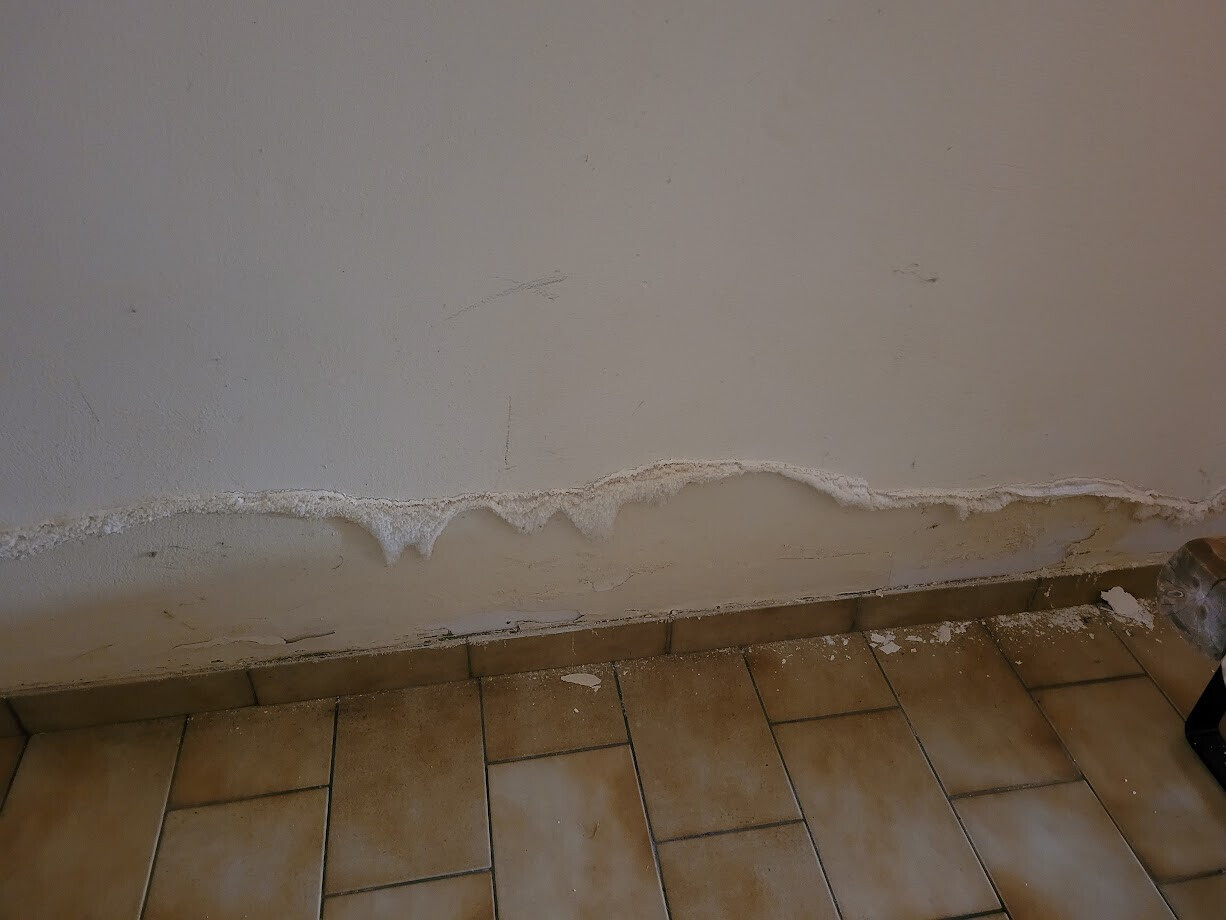 Wall with moisture damage: crumbling plaster at the lower edge above tiled floor