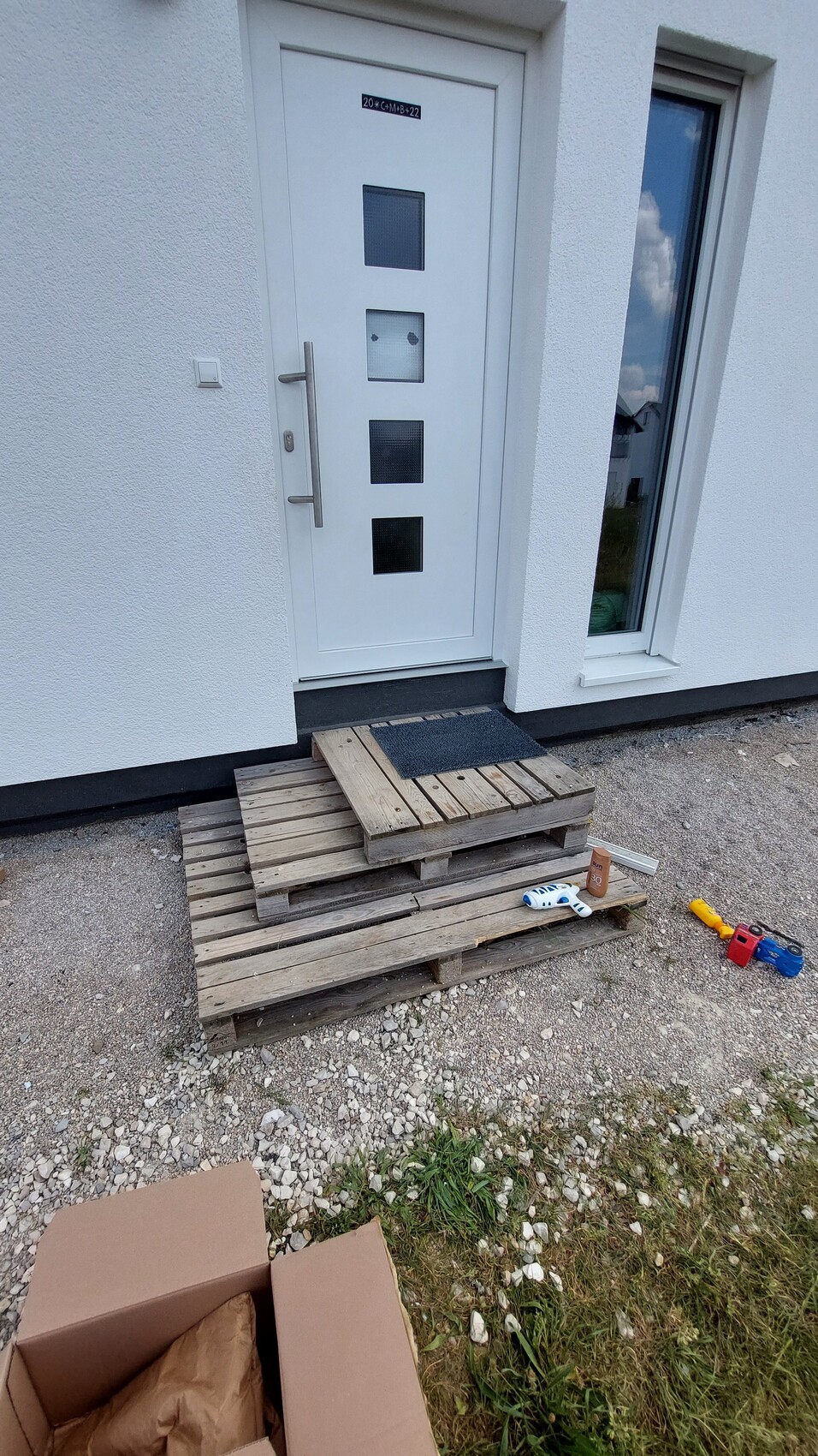 White front door with four square windows; pallet stairs in front of the entrance, toys next to it.