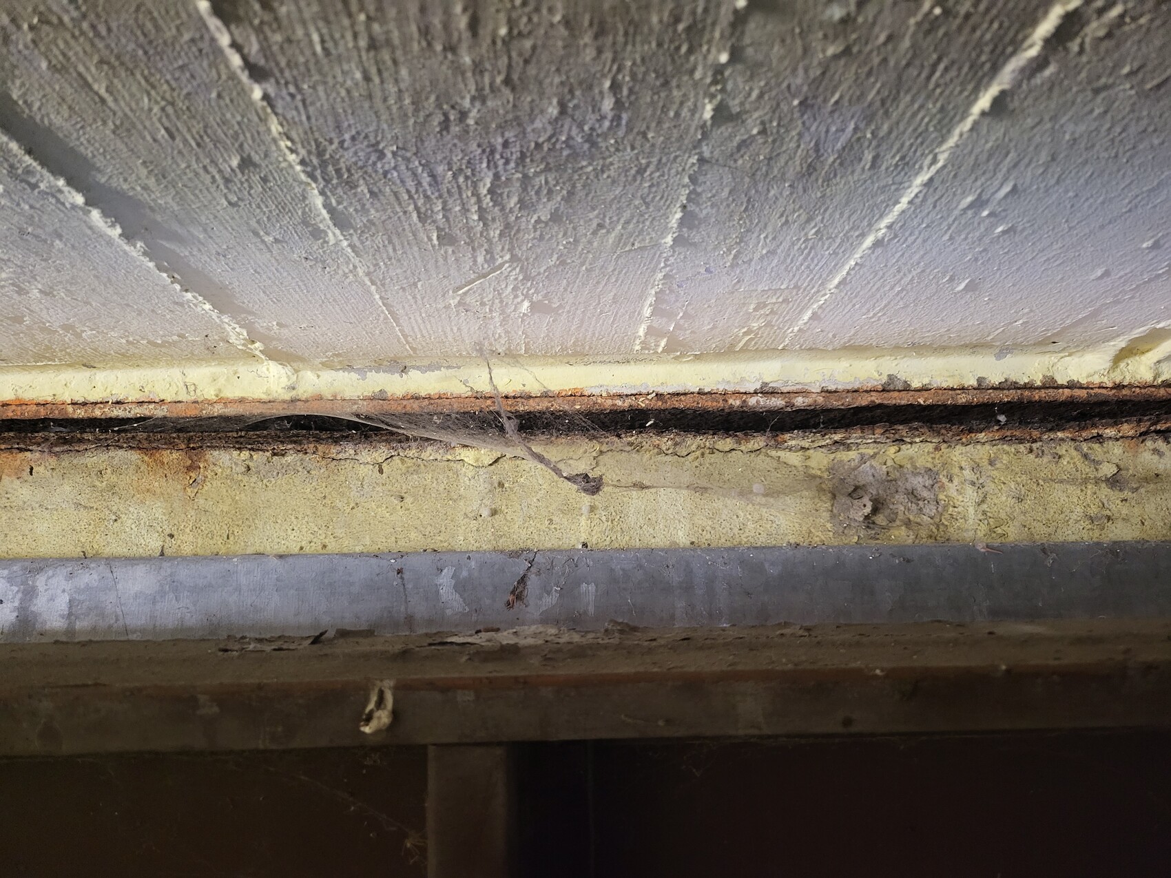 Close-up of a dusty gap between wall and floor, rusty metal edge, spider web.