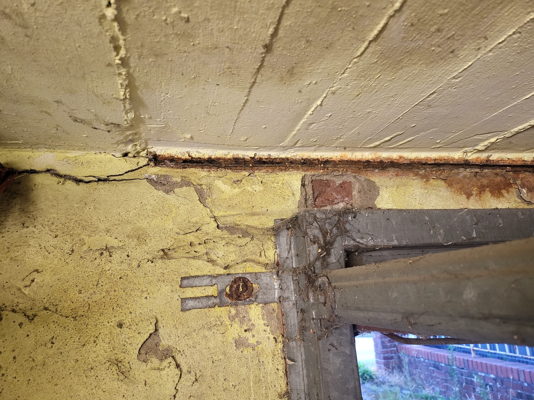 Crumbly yellow wall with cracks, rust stains and a rusty metal anchor on the window frame.