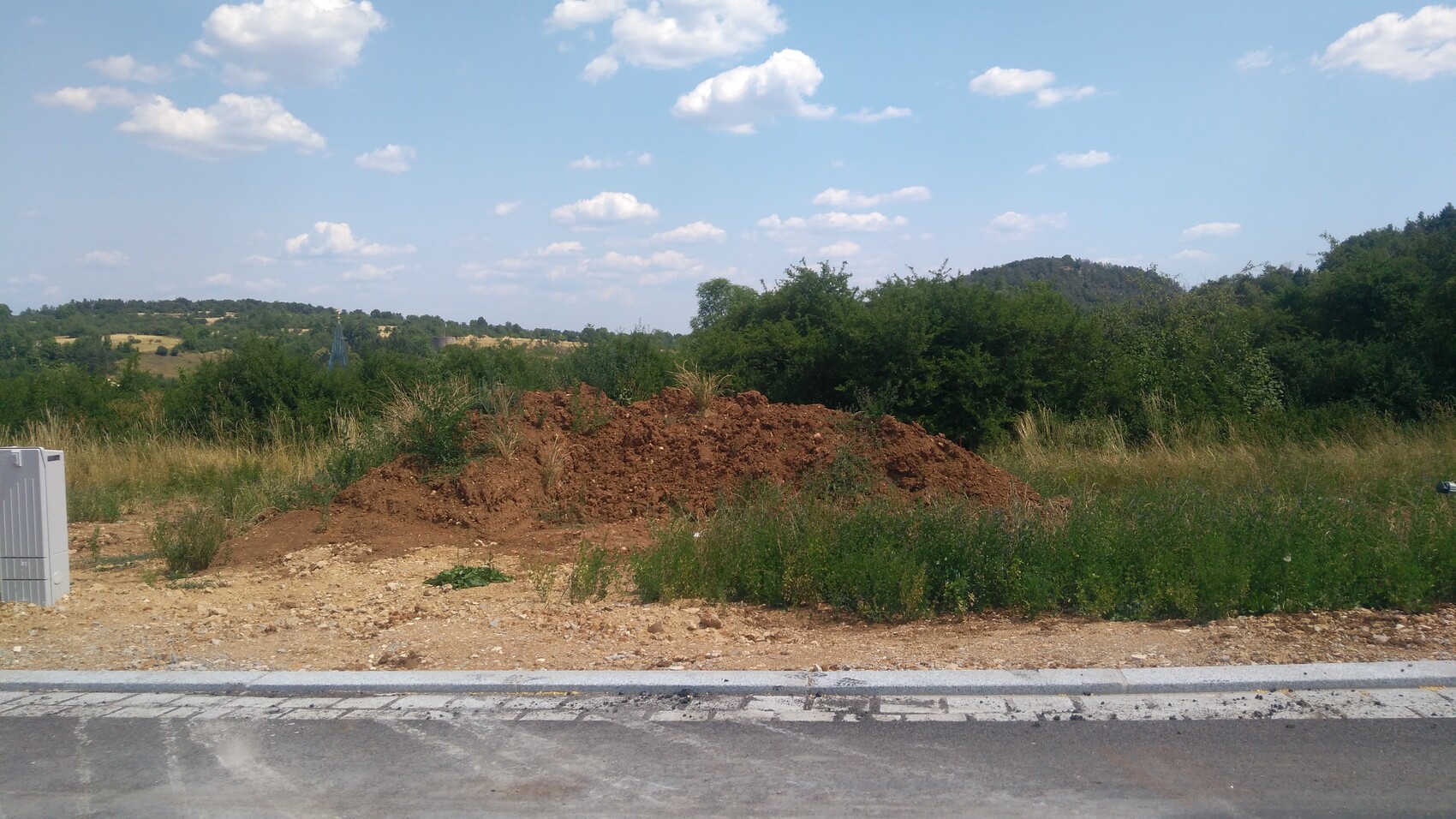 Large soil excavation mound at the roadside in a rural landscape with bushes and sky