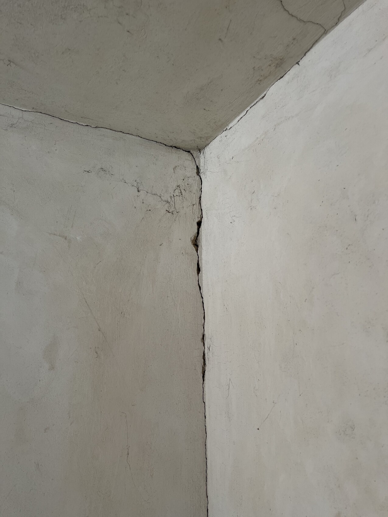 Corner of two plastered walls with vertical crack at the edge, ceiling visible.
