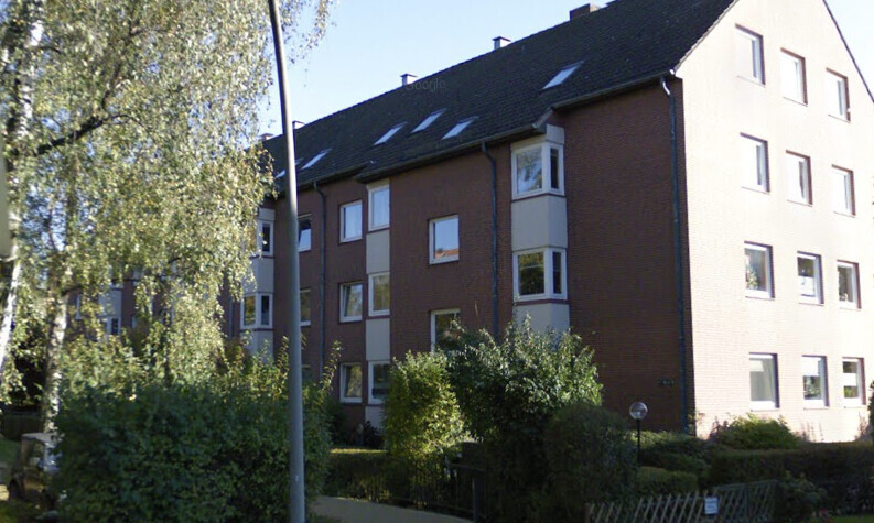 Multi-story brick building with white windows, surrounded by trees.